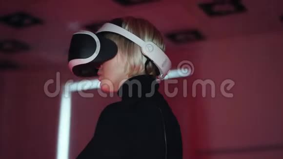一个年轻女子的特写镜头她戴着虚拟现实耳机站在一个充满红色和蓝色霓虹灯的游戏室里视频的预览图