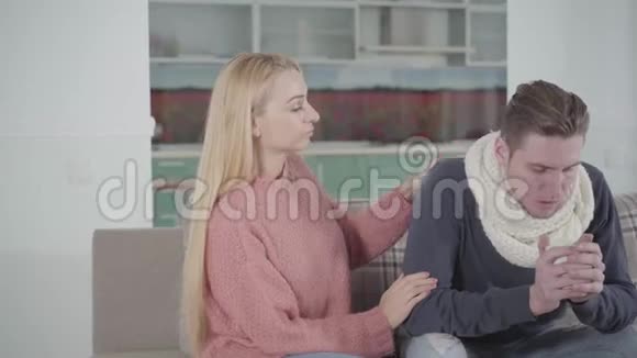 年轻的白种人女人一边爱抚丈夫一边喝热饮料照顾病人的妻子视频的预览图
