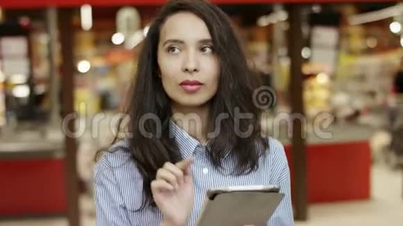 在超市里一个迷人的黑发女孩在她的平板电脑上列出购物清单列出要购买的物品人们视频的预览图