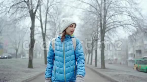 冬天的雾天穿着蓝色羽绒服和羊毛帽的年轻运动女子沿着小巷散步视频的预览图