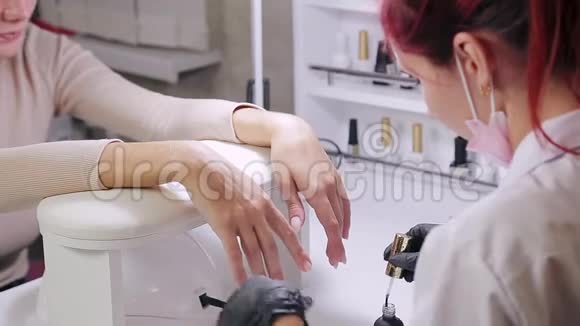 一家美容院带手套的女美甲师在涂胶前先把顾客的指甲刮掉视频的预览图