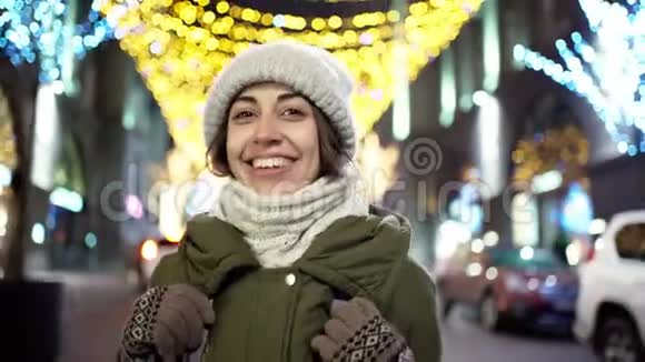 幸福微笑的年轻女子的特写夜像微笑的女人在许多灯光花环上走着夜城的街道视频的预览图