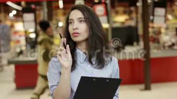超市里漂亮的女孩在她的文件夹上写下信息列出数字做笔记关闭视图视频的预览图