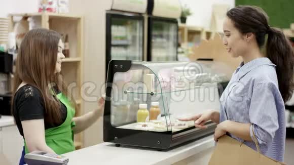 漂亮的年轻女人在咖啡店买甜甜点支付信用卡与友好的咖啡师无接触付款视频的预览图