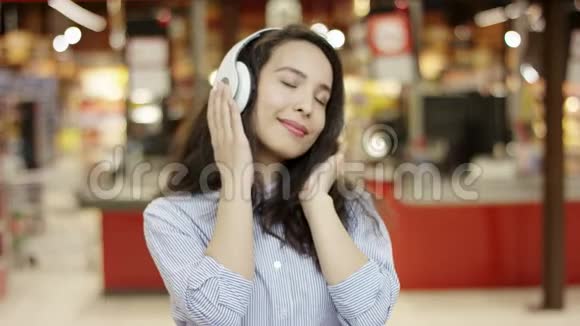 在超市里一位快乐的年轻漂亮的女士听着耳机里的音乐闭上眼睛微笑着享受着视频的预览图