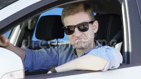 年轻人在他的车里放弃了拇指英俊的黑发男人在车窗里冷着脸蓝色屏幕色度键背景视频的预览图