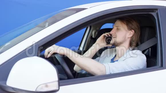 布鲁内特的家伙正在用手机说话开着一辆蓝色背景的车他很高兴也很满意司机视频的预览图