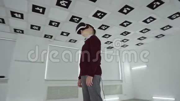 穿着棕色毛衣的小男孩正在用虚拟真人耳机环顾四周充满白色霓虹灯的空玩室视频的预览图