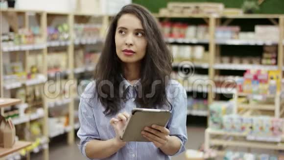 女顾客使用平板电脑查看超市的购物清单做出决定买什么看视频的预览图