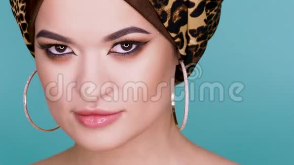 一个漂亮的年轻女子戴着一顶由豹纹织物制成的时尚头巾背景是蓝色视频的预览图