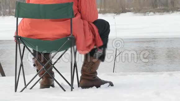 冬天一个渔夫坐在凳子上钓鱼背景中流淌的河流海岸被雪覆盖视频的预览图