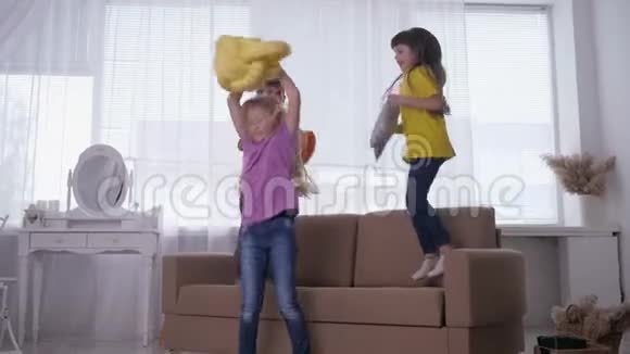 孩子们手里拿着枕头孩子们穿着五颜六色的T恤在明亮的房间里跳跃和旋转视频的预览图