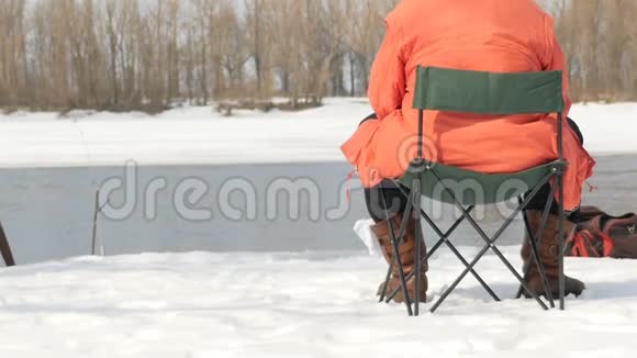 一个渔夫坐在凳子上在冬天钓鱼河流流动慢动作视频的预览图