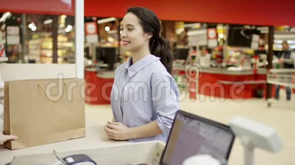 超市里漂亮积极的女顾客从柜台拿着购物袋谢谢收银员开心地笑着视频的预览图