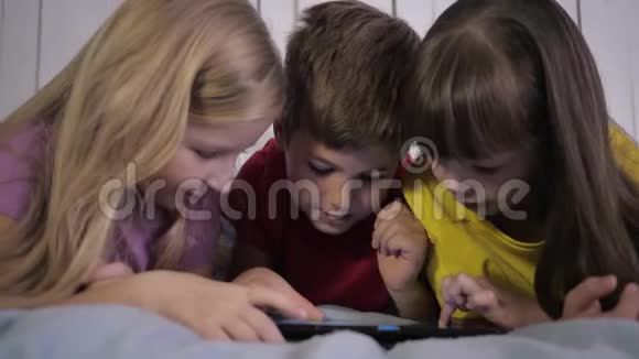 孩子们在假期的时候在家里玩得很开心现代的小女孩和穿多色t恤的男孩使用平板电脑视频的预览图