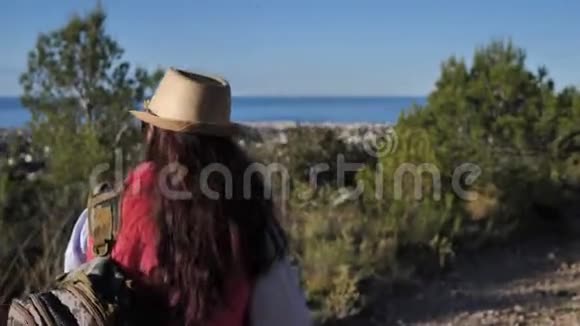 戴着帽子和太阳镜的女人走在山顶上环顾四周视频的预览图