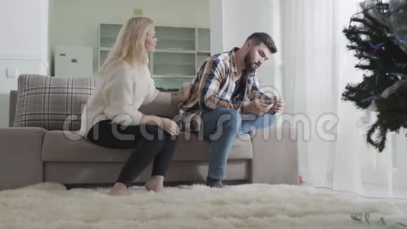 年轻的金发女人爱抚男人回来说话坐在沙发上背对着妻子或妻子的大胡子视频的预览图