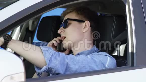 戴着太阳镜的布鲁内特男子正在用手机和绿色屏幕背景的汽车交谈他坐在里面视频的预览图