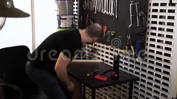 一个穿着黑色T恤的长胡子秃顶工人在他的车间里完成他的工作关掉老式收音机把工具挂在里面视频的预览图