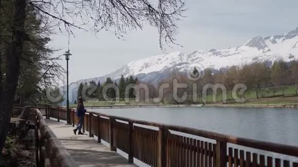 美丽的女孩站在木制长廊露台上欣赏风景优美的山湖和瑞士阿尔卑斯山一般视频的预览图