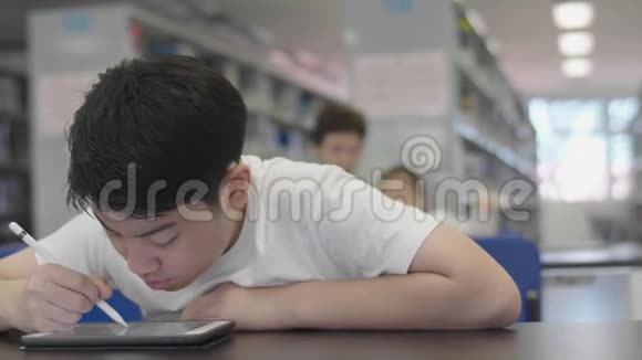 亚洲预科男孩使用平板电脑在图书馆视频的预览图