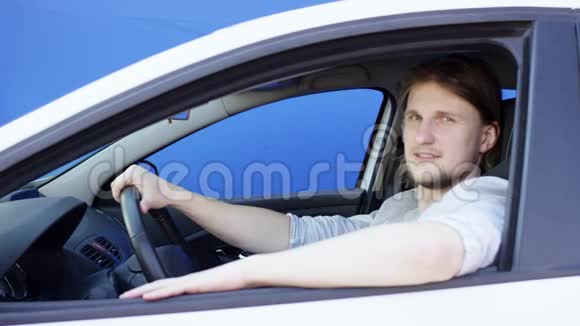 满意和冷静的家伙正在看着相机和眨眼布鲁内特先生坐在他那辆带蓝色的白色车里视频的预览图