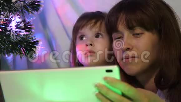 圣诞节晚上妈妈和女儿在平板电脑上玩和看动画片在一个带花环帐篷里的孩子房间里视频的预览图