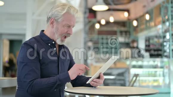老人在咖啡馆的平板电脑上庆祝成功视频的预览图
