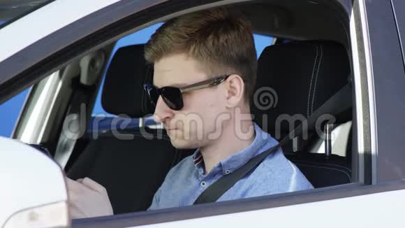 年轻人坐在蓝色背景的车里发短信戴墨镜的帅哥在聊天视频的预览图