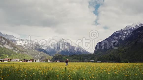 在风景如画的山谷里一个穿着花大衣的快乐女人走在蒲公英地上浪漫梦幻的心情视频的预览图