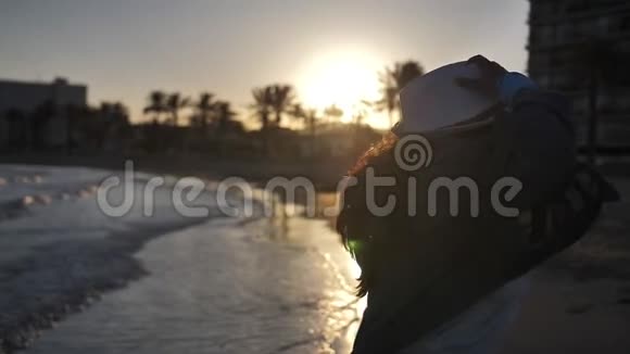 快乐的旅行者女人戴着帽子在海上欢乐日落在自己的慢动作中旋转视频的预览图