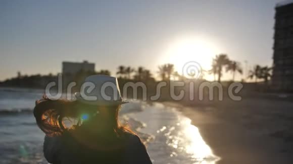 日落时戴帽子的女人站在海岸线上慢动作视频的预览图