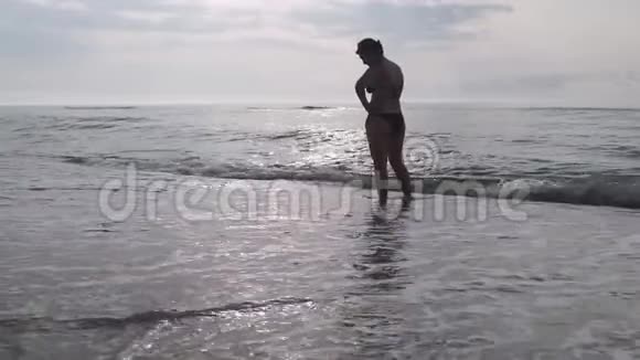 一位剪影中的女士欣赏着海滩上海水中的一个美丽而美丽的日出视频的预览图