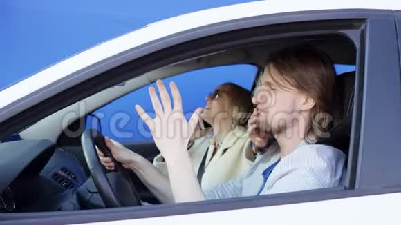 Brunette男子和金发女子乘坐蓝色背景的白色汽车旅行年轻的司机大声喊叫视频的预览图
