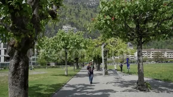 瑞士的一位身穿花纹外套戴着墨镜的女士在一条绿色公园小巷里漫步视频的预览图