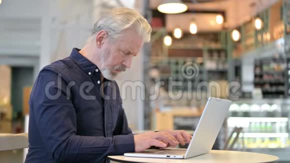 有头痛的老人在咖啡厅使用笔记本电脑视频的预览图