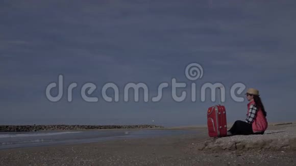 女游客带着一个手提箱坐在海边的海岸线上在埃宁旅游理念复制空间视频的预览图