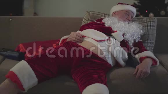 坏圣诞老人睡在沙发上挠肚子空瓶子躺在他旁边的沙发上酗酒视频的预览图