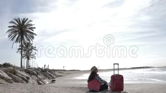 女游客带着一个手提箱坐在海边的海岸线上视频的预览图