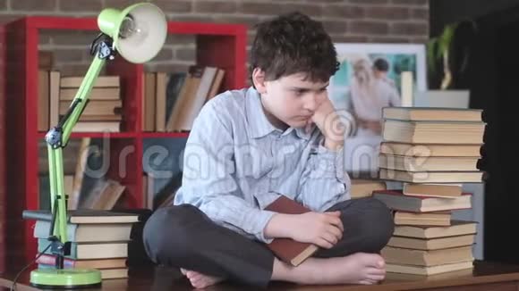 男生盘腿坐在书桌上手里拿着一本打开的书很无聊视频的预览图