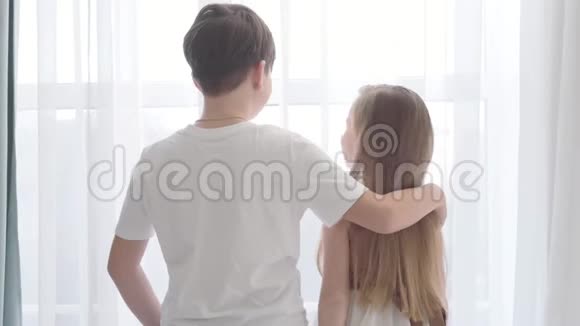 从后面看白人男孩和女孩站在一起看窗外穿着白色T恤的布鲁内特视频的预览图