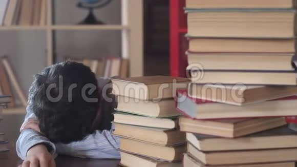 男生睡在桌子上在学校里把一个孩子抱在一堆书里视频的预览图