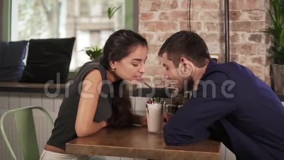 漂亮的年轻夫妇在咖啡馆里坐在木桌旁用吸管喝奶昔快乐的夫妻视频的预览图