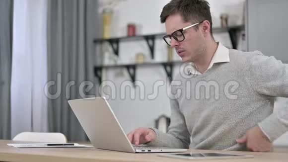 有脊背疼痛的年轻人在笔记本电脑上工作视频的预览图