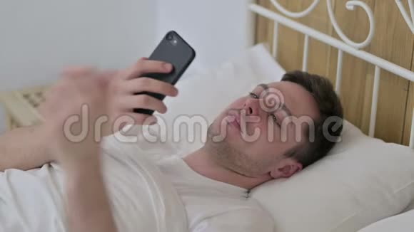 在床上讲智能电话的年轻人视频的预览图