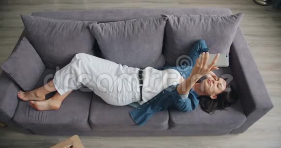高角度观看可爱的女孩自拍与智能手机躺在沙发在家里视频的预览图