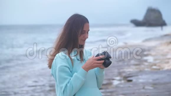 肖像时髦的女人是一个专业摄影师与相机她在黄昏时在海洋背景上拍照4k视频的预览图