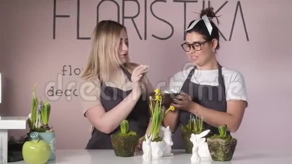 两个穿围裙的女朋友在工作场所玩得很开心一篮子彩绘的复活节彩蛋视频的预览图