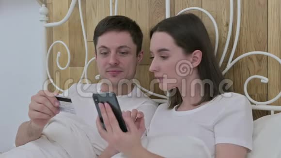 网上支付床上智能手机的年轻夫妇视频的预览图