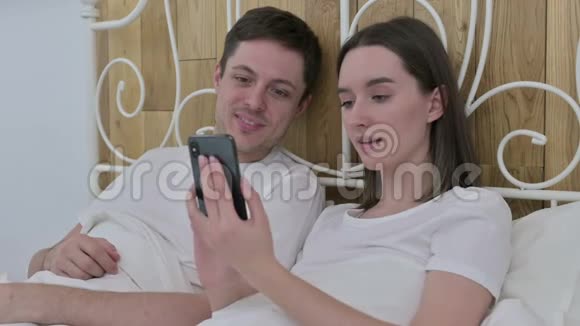 年轻夫妇在床上用智能手机聊天视频的预览图